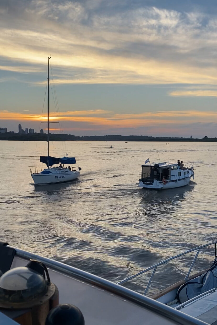 Velero y lancha navegando al atardecer frente al skyline de Paraná